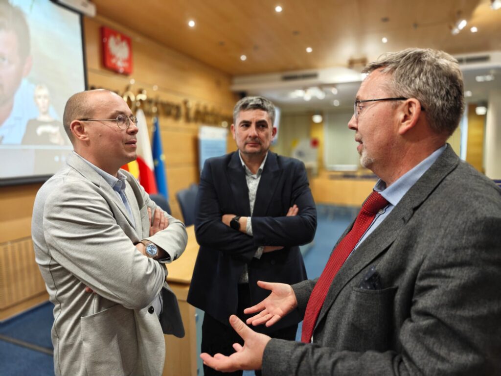 1.	Trzej mężczyźni prowadzący dyskusje. W tle widoczny rzutnik, na którym wyświetla się obraz. 