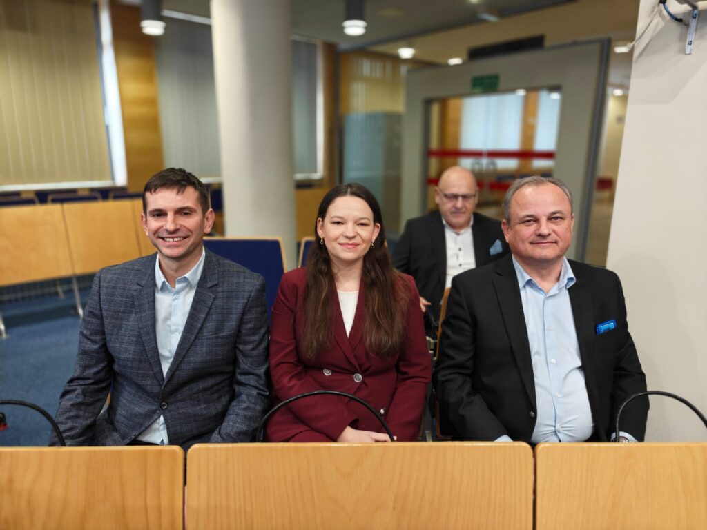 10.	Trzy osoby siedzą w sali konferencyjnej: mężczyzna, kobieta i kolejny mężczyzna, wszyscy skupieni na rozmowie.  