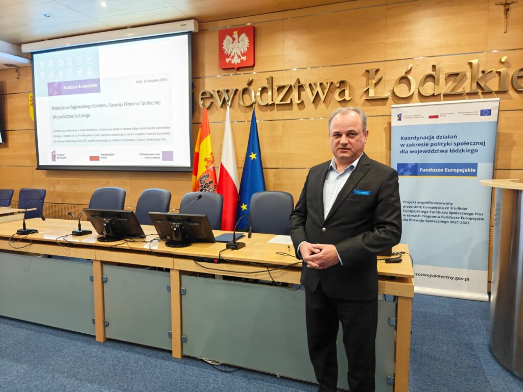 4.	Mężczyzna w eleganckim garniturze w pozycji stojącej przed salą konferencyjną przemawia.   