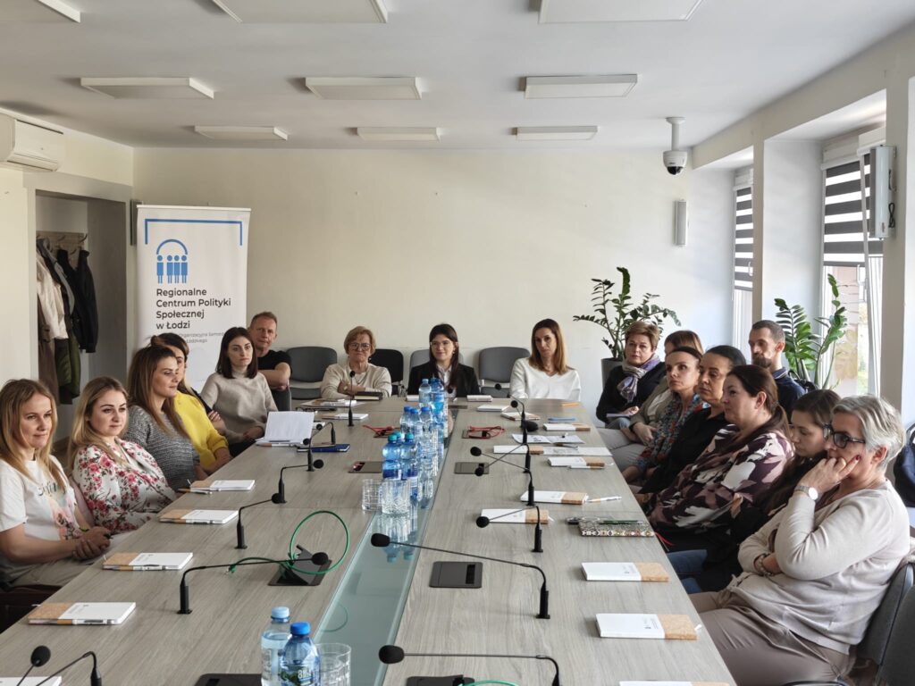 Uczestnicy siedzą przy stole konferencyjnym w sali.  