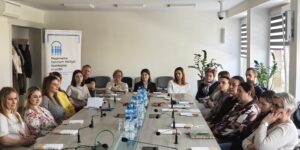 Uczestnicy siedzą przy stole konferencyjnym w sali.