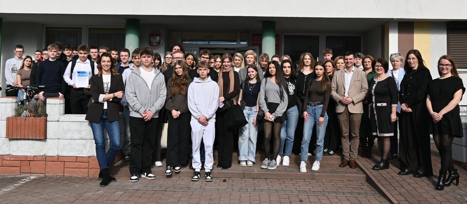 Grupowe zdjęcie młodzieży i organizatorów przed budynkiem szkoły podczas spotkania upowszechniającego ekonomię społeczną w Radomsku