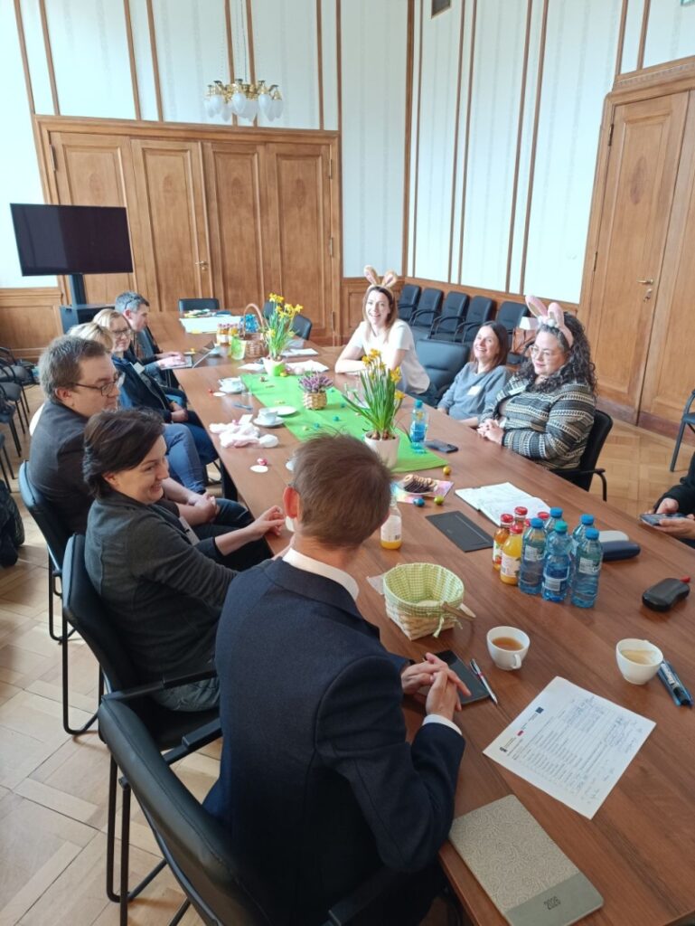 Osoby zgromadzone przy stole, uczestniczące w dyskusji w przyjaznej atmosferze.