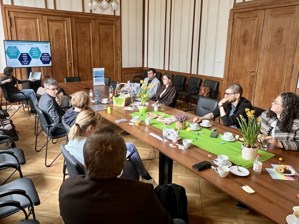 Osoby siedzące przy stole w sali spotkań, prowadzące rozmowę