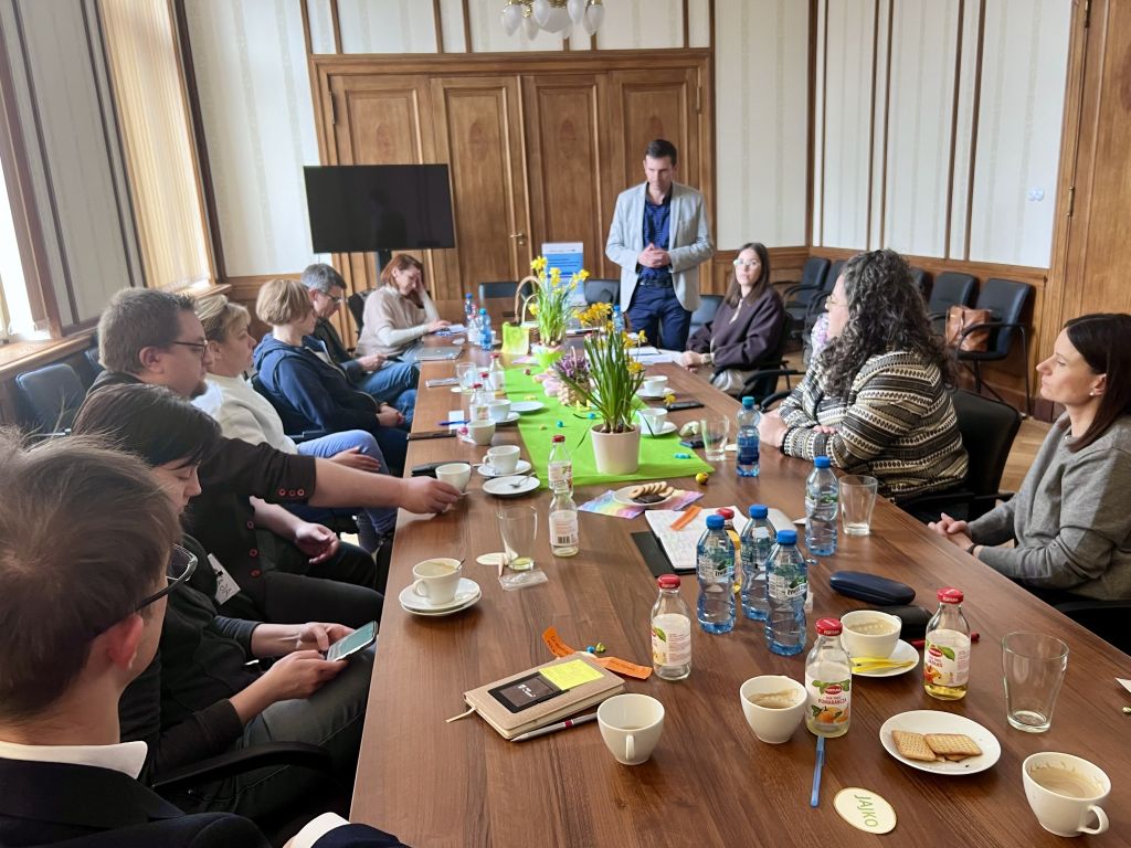 Zespół ludzi siedzący przy stole, zaangażowany w rozmowę i współpracę