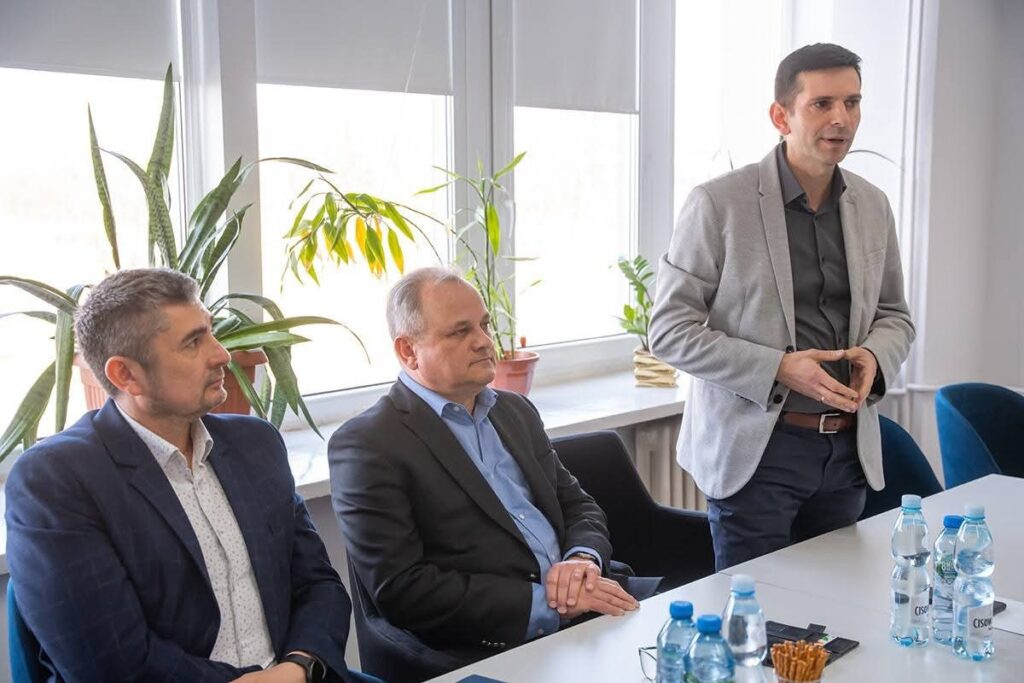 Trzech mężczyzn siedzi przy stole, obok nich znajdują się butelki wody.