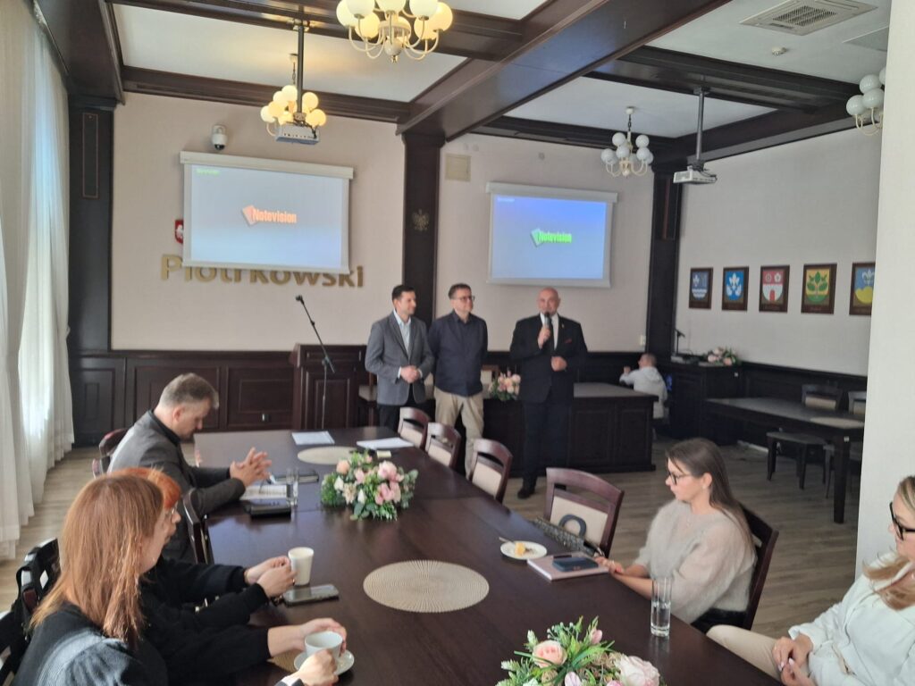 Grupa ludzi siedzi przy stole w sali konferencyjnej podczas spotkania.
