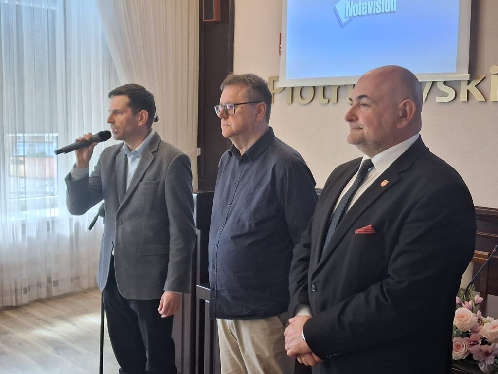 Trzech mężczyzn stoi obok siebie przy podium, każdy z nich ma poważny wyraz twarzy.