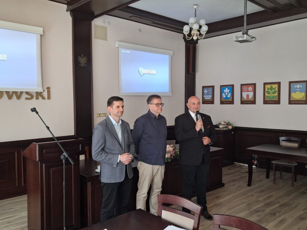 Trzech mężczyzn stoi przed podium w sali.