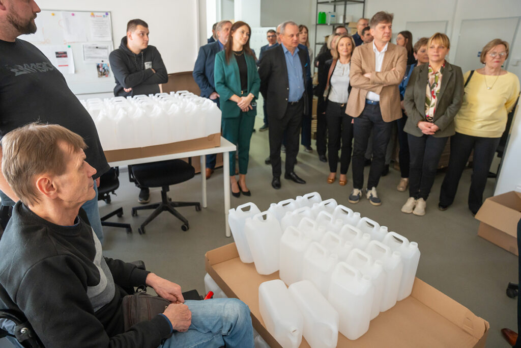 Grupa ludzi stoi wokół stołu z plastikowymi pojemnikami.