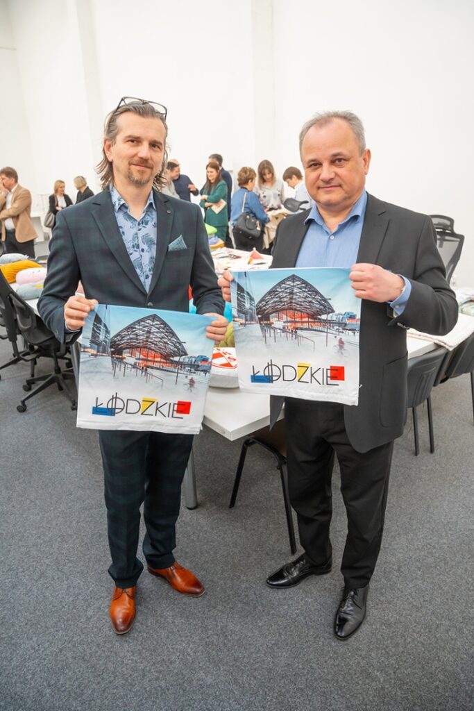 Dwaj mężczyźni trzymający plakaty podczas wydarzenia, uśmiechając się do kamery.