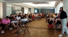 Grupa ludzi siedzących na krzesłach w sali, rozmawiających ze sobą w przyjaznej atmosferze