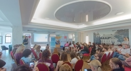 Grupa ludzi siedzących na krzesłach w sali, wsłuchana w wykład