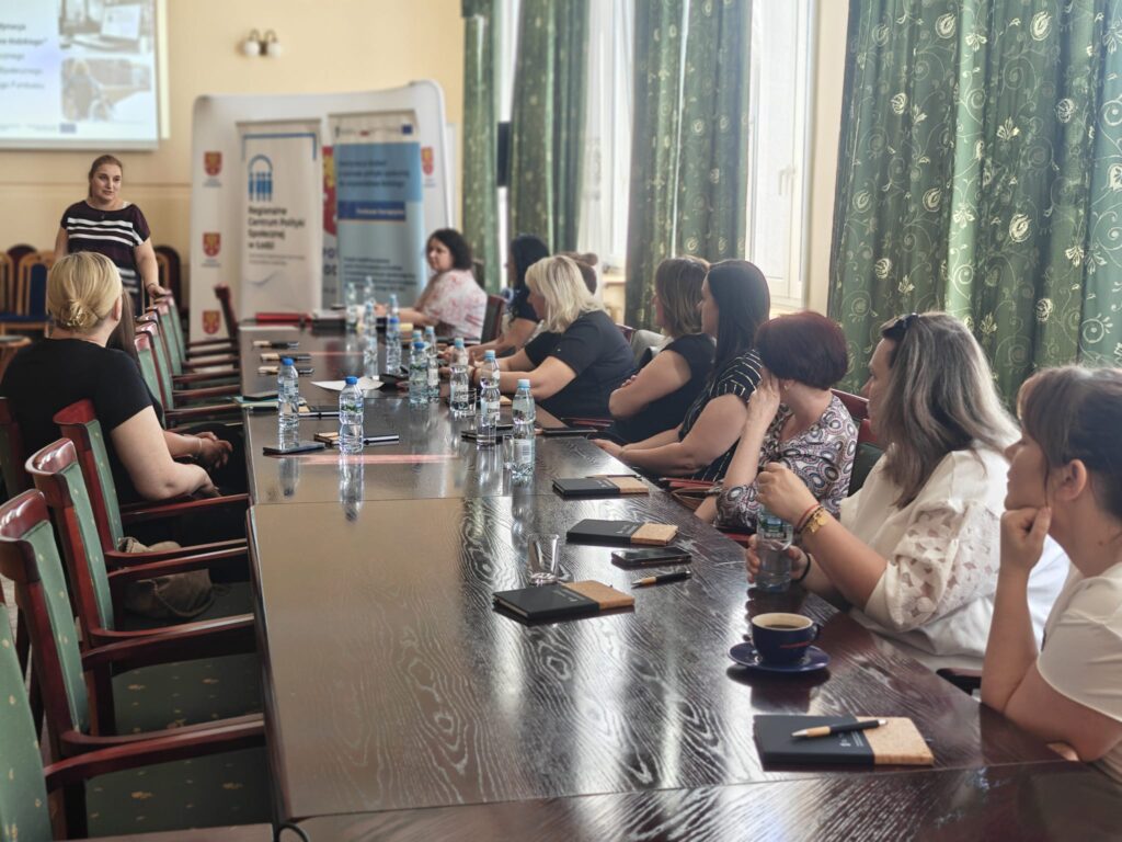 Grupa ludzi siedzi przy długim stole, rozmawiając i dzieląc się pomysłami