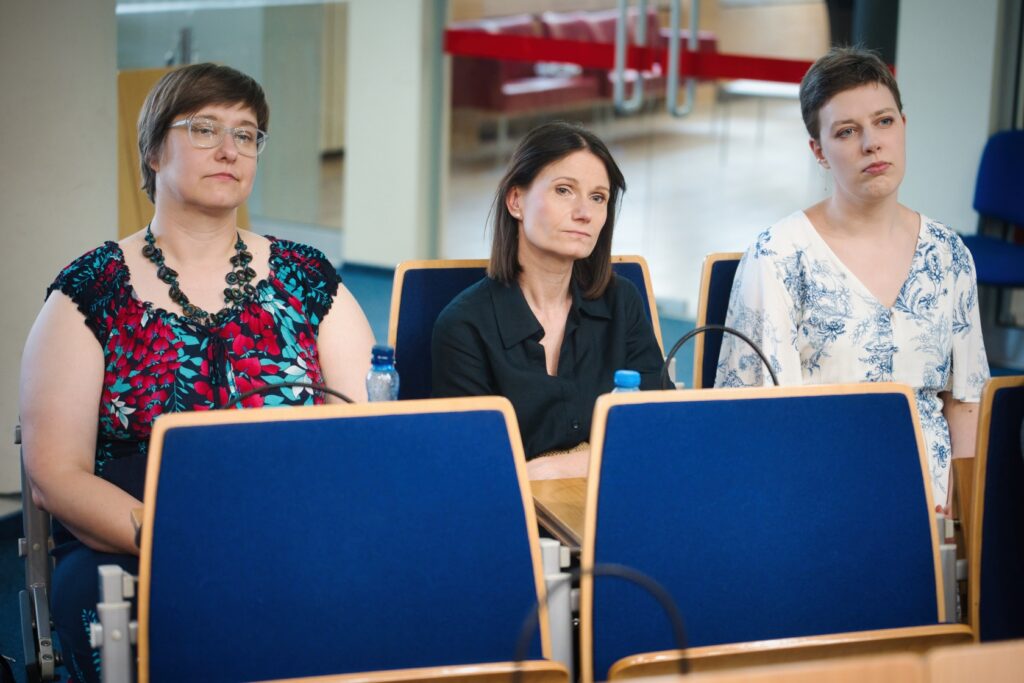 Trzy kobiety siedzące przed mikrofonem w sali konferencyjnej, prowadzące dyskusję