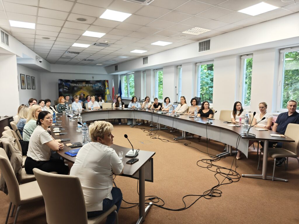 uczesticy siedzący przy okrągłym stole wsłuchani w wykład