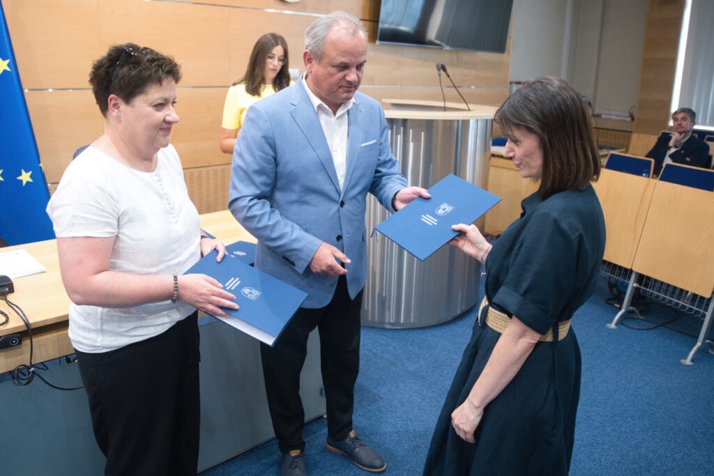 wie osoby w pozycji stojącej, z niebieską teczką w tle, prezentujące przyjazną postawę.