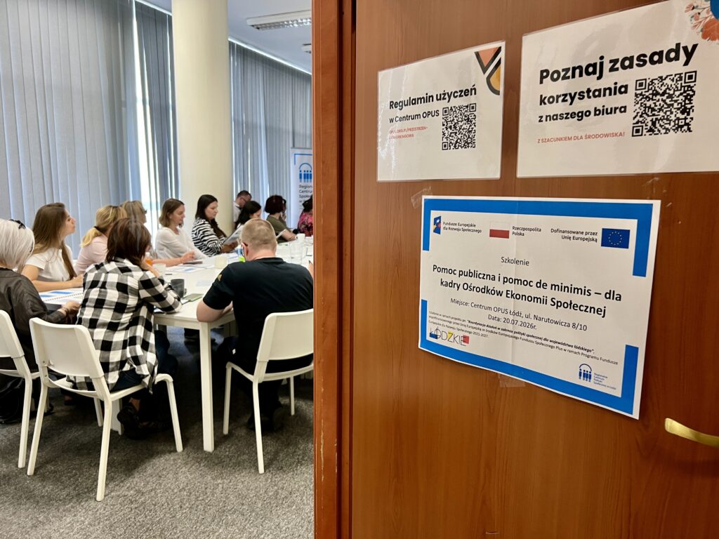 Otwarte drzwi do pomieszczenia, w którym grupa osób siedzi przy stole.